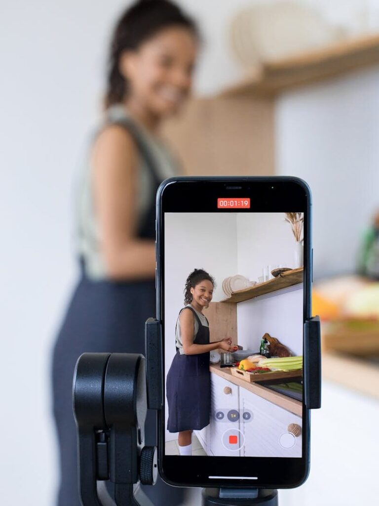 Woman vlogging her cooking tutorial in a kitchen using smartphone on a tripod.